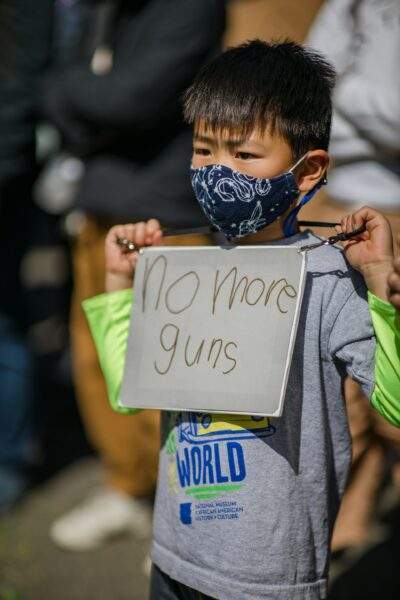 child holding a protest sign "no more guns"