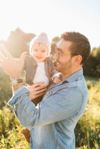 father and baby smiling in a field, backlit by the sunset